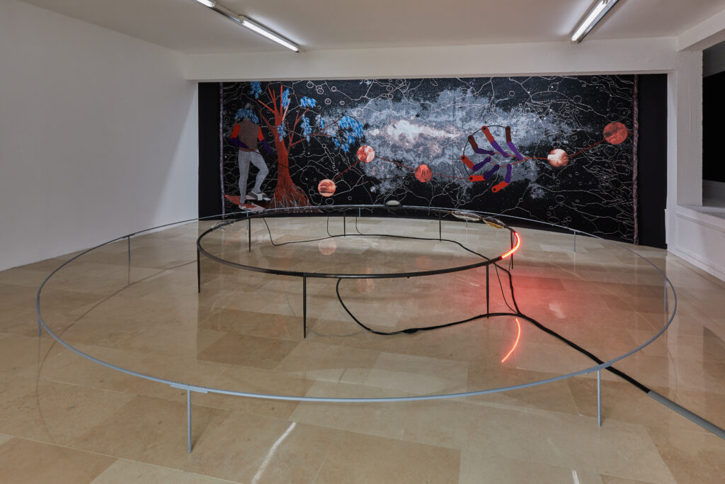 une tapisserie dans le fond avec une installation en métal, néon et pierre