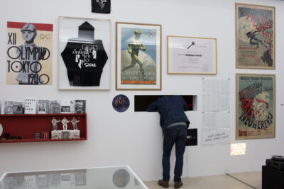 vue de l'exposition avec un visiteur qui regarde au travers d'un trou dans le mur