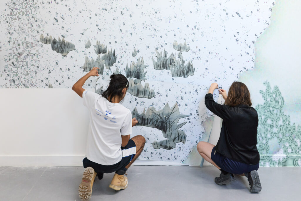 Deux artistes appliquent un papier peint sur un mur