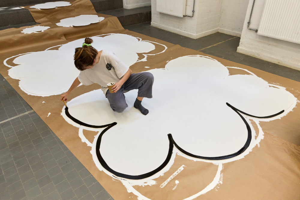 Un artiste peint accroupie au milieu de son oeuvre, un grand nuage blanc