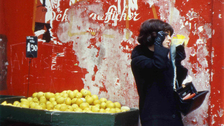 Un étale de citron et une femme à droite de l'image sur fond de mur décrépi rouge